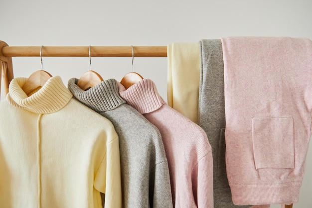 Close up view of pink beige and grey knitted soft sweaters and pants hanging on wooden rack