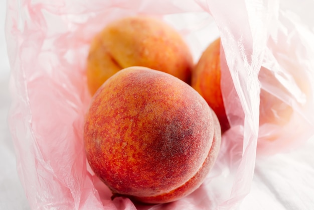 Close-up view plastic bag with natural freshly picked organic peach fruits on a textile background.