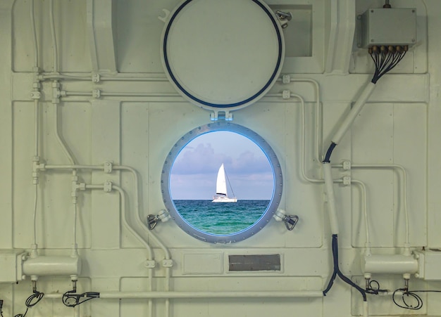 Close up view of porthole on a cruise ship with ocean and yacht view