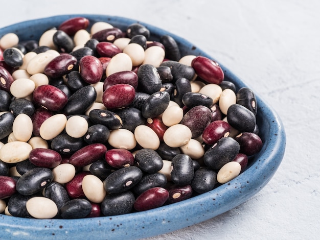 Close up view of raw mixed beans in blue plate on gray concrete background mixed of black red and white beans with copy space