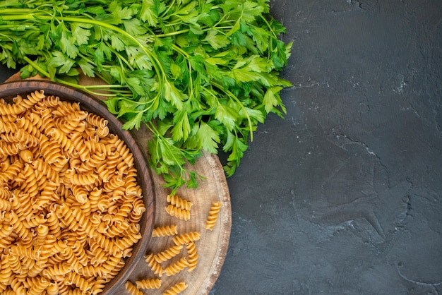 Close up view of raw pastas inside and outside brown pot green bundle on dark blue color background