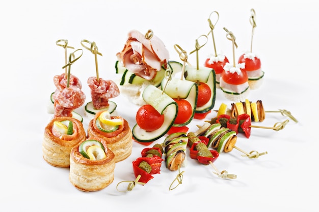 Close-up view set of canapes with vegetables, salami, seafood, meat and decoration on white plate