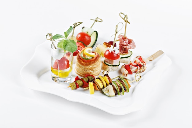 Close-up view set of canapes with vegetables, salami, seafood, meat and decoration on white plate