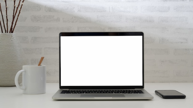 Close up view of simple workplace with  laptop , coffee cup and phone on white desk