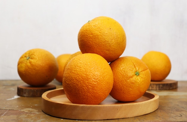 Close up view of some fresh navel oranges with wooden plate on wooden table