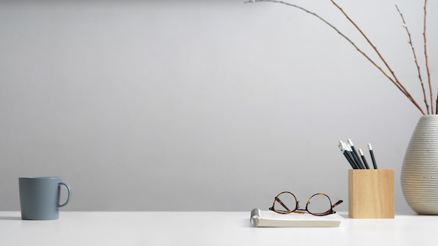 Close up view of study table with stationery, eyeglasses, notebook, mug, decoration and copy space in home office