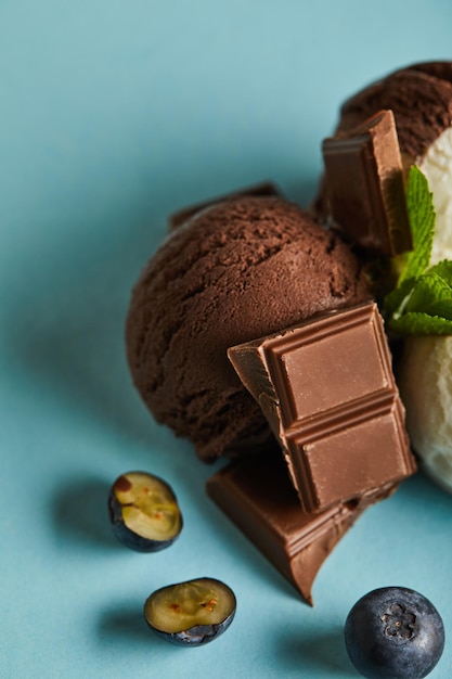 Close up view of tasty brown ice cream with berries chocolate and mint on blue background