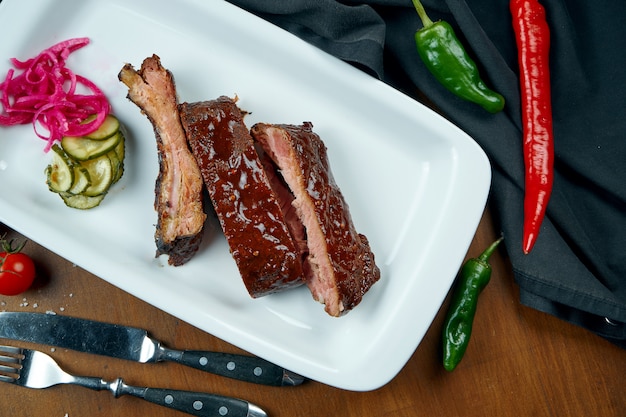 Close up view on tasty delicious bbq cooked ribs with barbecue sauce in white plate on wooden table. Classical american Barbecued Pork in composition with ingredients