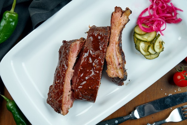 Close up view on tasty delicious bbq cooked ribs with barbecue sauce in white plate on wooden table. Classical american Barbecued Pork in composition with ingredients