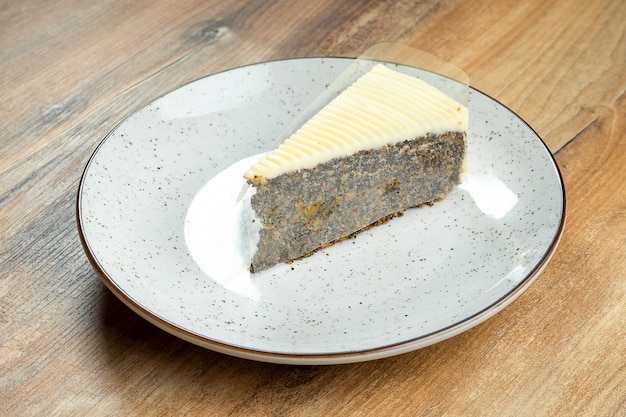 Close up view on tasty slice Poppy seed cake in white plate on wooden background. Delicious cream cake. Sweet dessert after lunch.