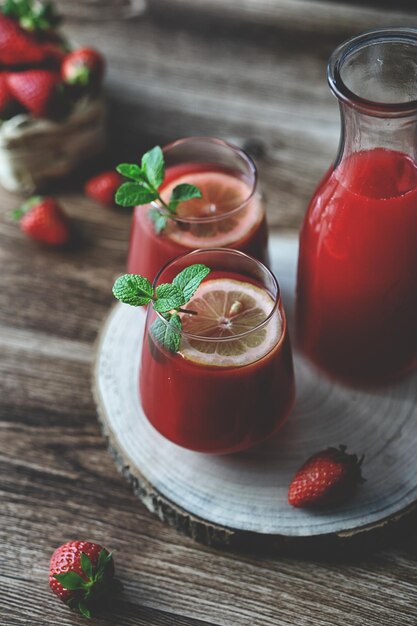 Photo close up view of two glasses of homemade refreshing strawberries juice nectar drink and mint