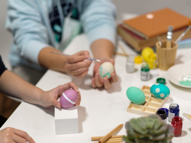 Close up view of two people hands painting on Easter eggs with paint tools on the table