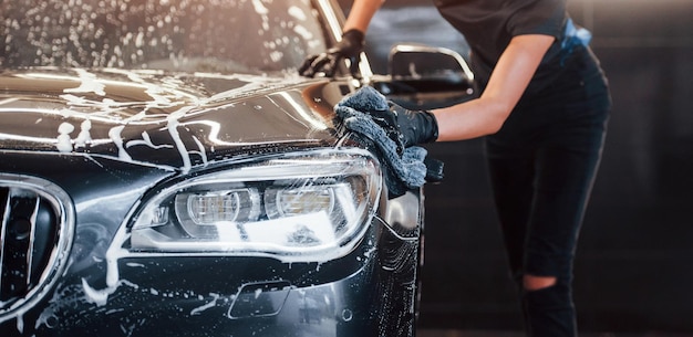 Close up view of vehicle getting wiped Modern black automobile get cleaned by woman inside of car wash station