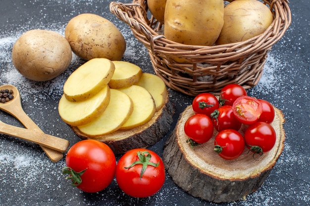 Close up view of whole and chopped fresh potatoes and tomatoes on wooden board pepper on black white mix colors background