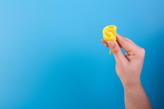 Close up view of woman holding yellow menstrual cup isolated over blue background woman's period