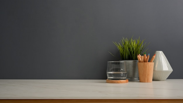 Close up view of worktable with a glass of water, stationery, vase, plant pot and copy space in home office