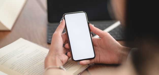 Close-up view of young businesswoman working on her project while using smartphone in comfortable office