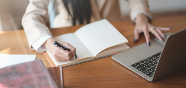 Close-up view of young businesswoman working on her project and writing her ideas in notebook in comfortable office