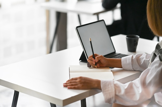 Close-up view of young businesswoman working on his plan writing the idea on notebook with digital tablet.