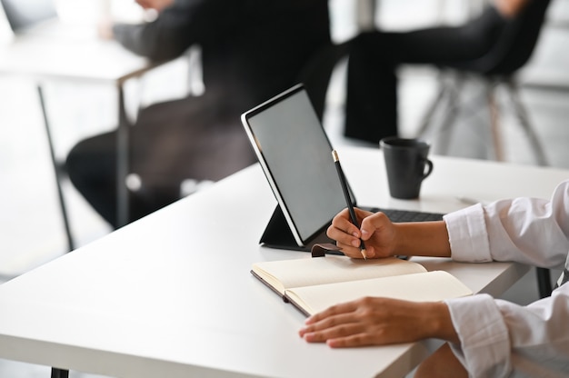 Close-up view of young businesswoman working on his plan writing the idea on notebook with digital tablet.