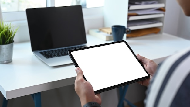 Close up view of young man freelance working with laptop and using digital tablet at home office