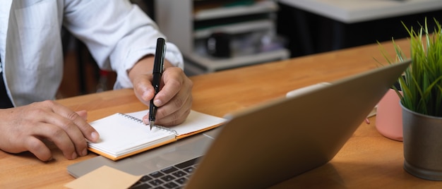 Close-up view of young man writing on notebook while working in office room