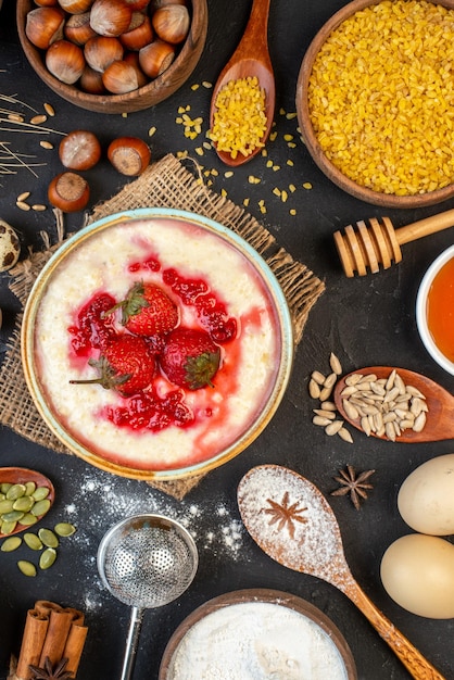 Close up view of yummy breakfast served with strawberries jam in a bowl and honey eggs flour sugar spoons on dark color background