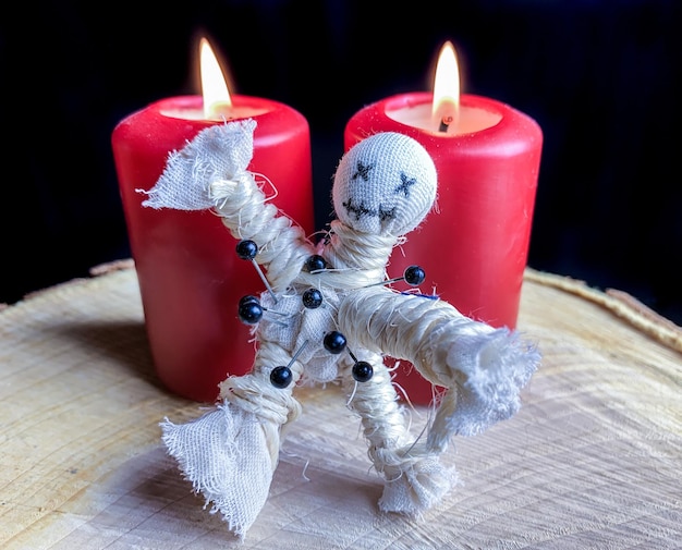 Photo close-up of voodoo doll by lit candles on table