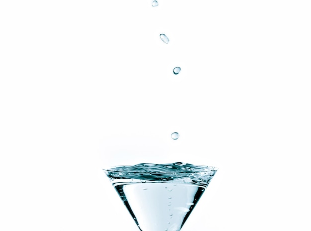 Close-up of water drop falling into a glass on white background.