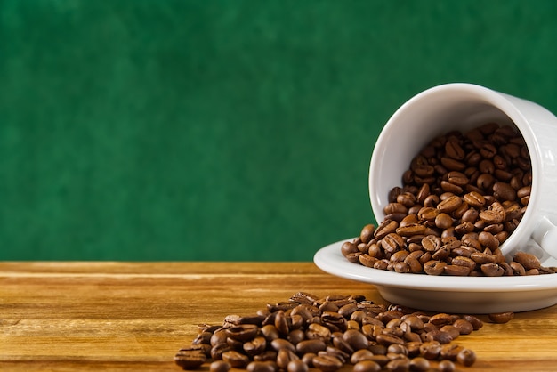 close up white coffee cup full of coffee beans on dark green background