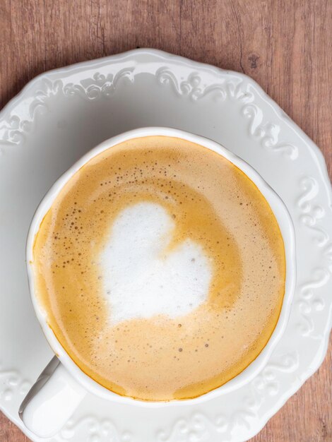 Close up white coffee cup with heart shape latte art on wood table at cafe