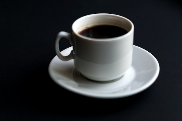 Close up of white cup of coffee on black background. Soft focus