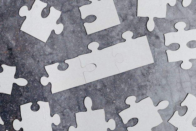 Close-Up White Jigsaw Pattern Puzzle Pieces To Be Connected With Missing Last Piece Positioned On A Flat Lay Background With Different Texture And Paper Supplies Accesories