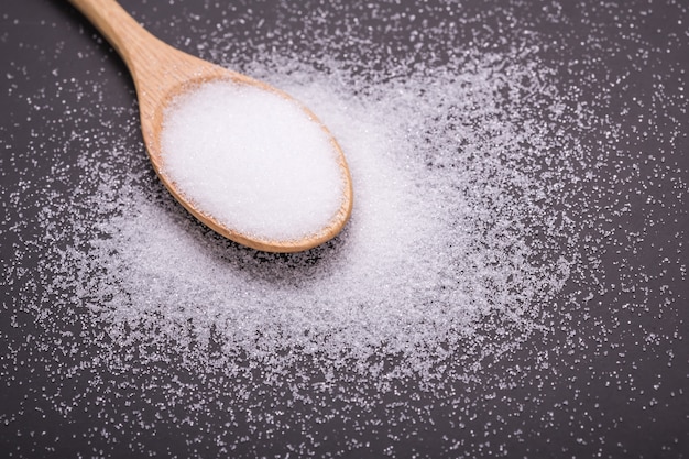 Close up white salt in wooden spoon and doctor stethoscope on black stone table