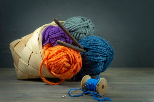 Close up of wicker basket with colorful balls of yarn and knitting needles on wooden background