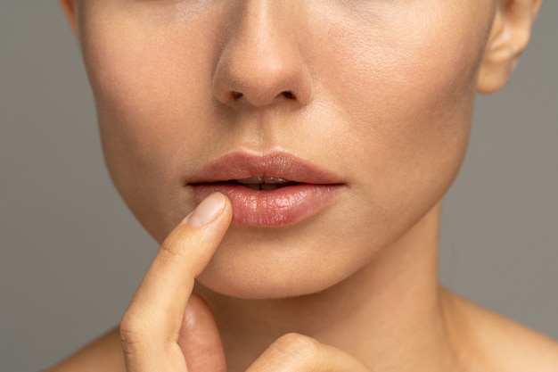 Close up of woman applying moisturizing nourishing balm to her lips with her finger