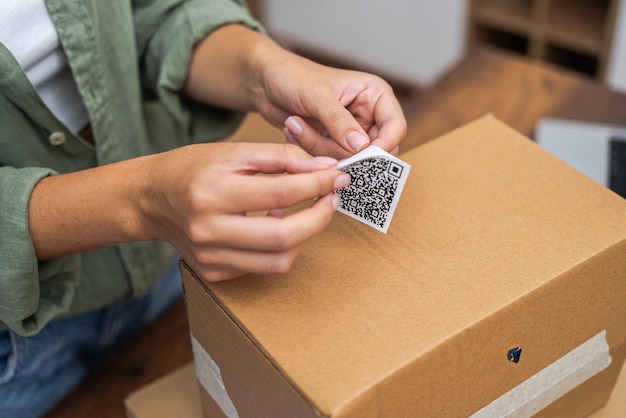 Photo close up woman attaches qr code sticker to cardboard parcel to return and receive a refund