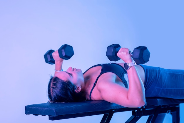 Close up of a woman bench pressing with two dumbbells