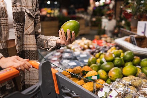 Close up of woman choosing ripe mango at supermarket