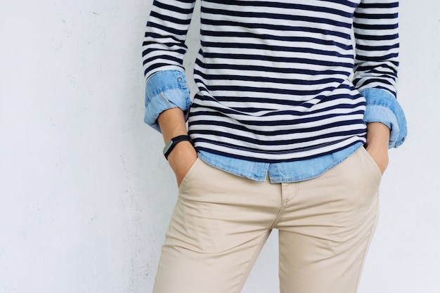 Close-up of a woman in a denim shirt, striped t-shirt and beige pants with a fitness tracker on hand