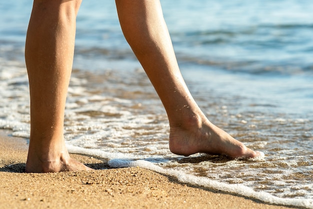 Close up of woman feet walking barefoot on sand beach in sea water