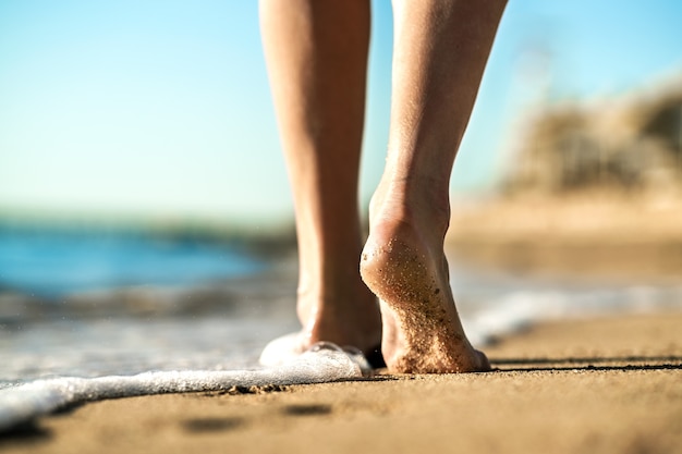 Close up of woman feet walking barefoot on sand leaving footprints on golden beach. Vacation, travel and freedom concept. People relaxing in summer.