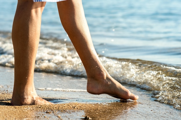 Close up of woman feet walking barefoot on sand leaving footprints on golden beach