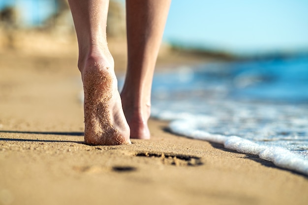 Close up of woman feet walking barefoot on sand leaving footprints on golden beach