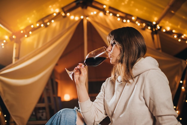 Close up of Woman freelancer drinking wine sitting in cozy glamping tent in autumn evening Luxury camping tent for outdoor holiday and vacation Lifestyle concept