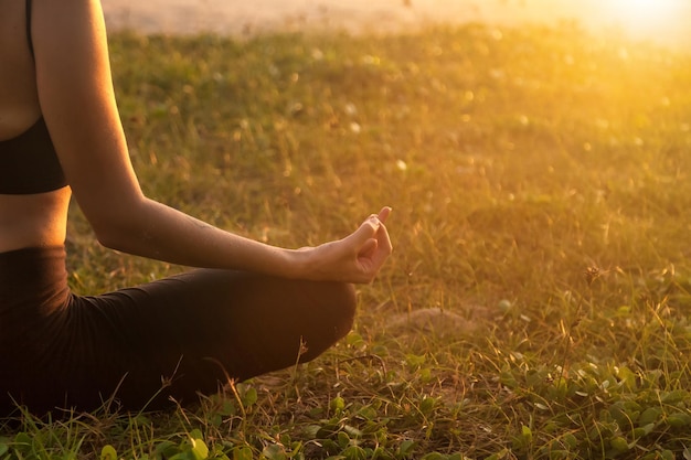 Close up woman hand does yoga in lotus posture on tropical sea coast or ocean beach outdoors at sunset