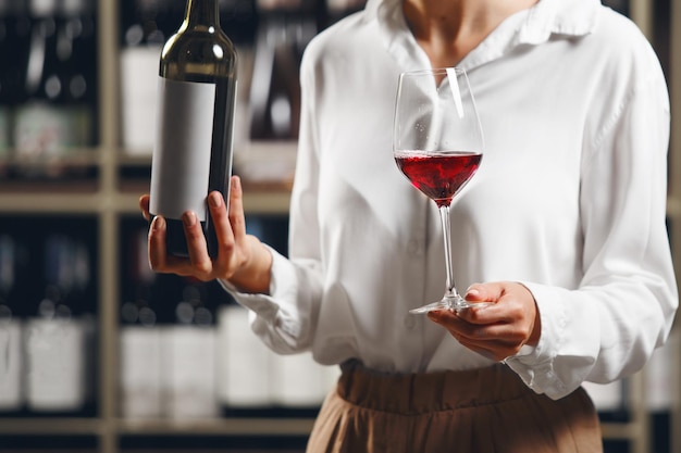 Close up woman hand hold bottle and glass with poured red wine on cellar background