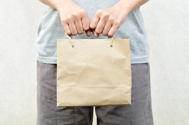 close up of woman hand holding blank brown paper bag package on white background