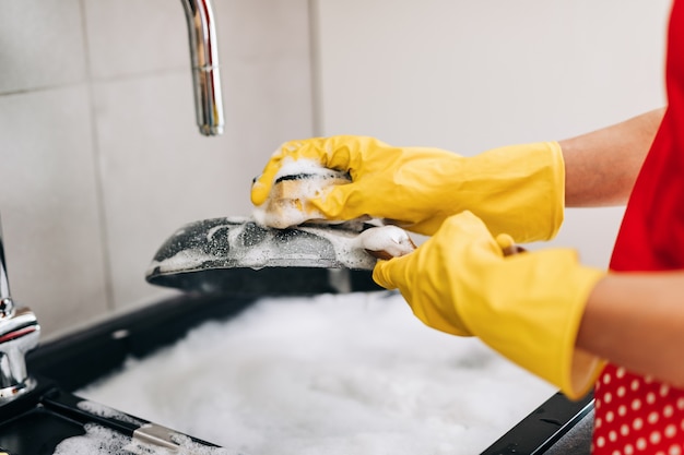 Close up of woman hand in yellow protective rubber gloves washing dishes in the kitchen.