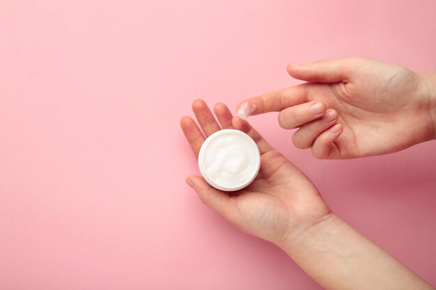 Close up woman hands holding bottle of white face cream touching it with finger on pink background Skin care